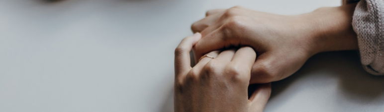 Closeup of hands folded together on a table.