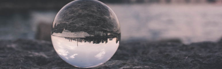 Glass sphere on a dark sandy beach, reflecting the beach.