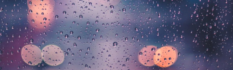 image of raindrops on glass with vehicle lights behind