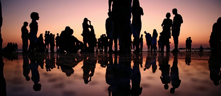 silhouette of group of people at sunset standing over and reflecting in water