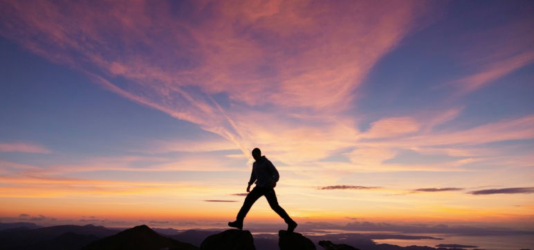 silhouette of man hiking at sunset over an indigo and violet sky